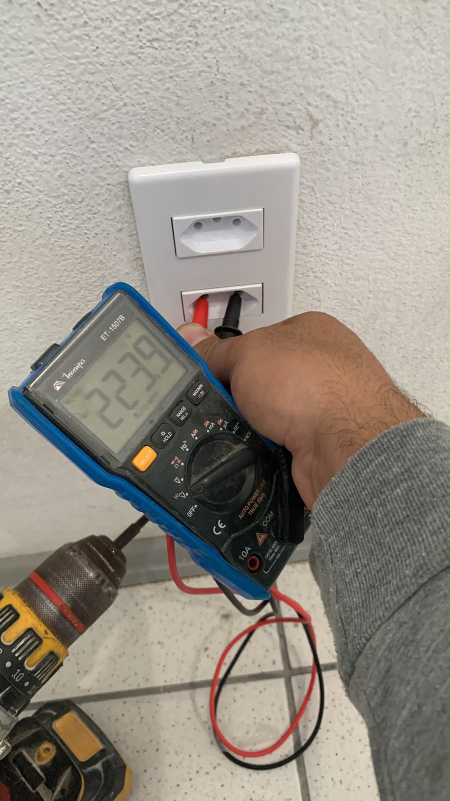 Tomada sendo medida com multímetro, marcando 223,9 volts